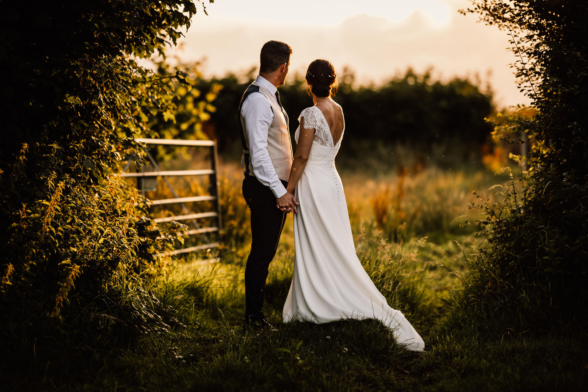 Golden hour wedding portrait of newlyweds in the countryside looking away from the camera and to the horizon. By Chris Armstrong Photography in Cornwall