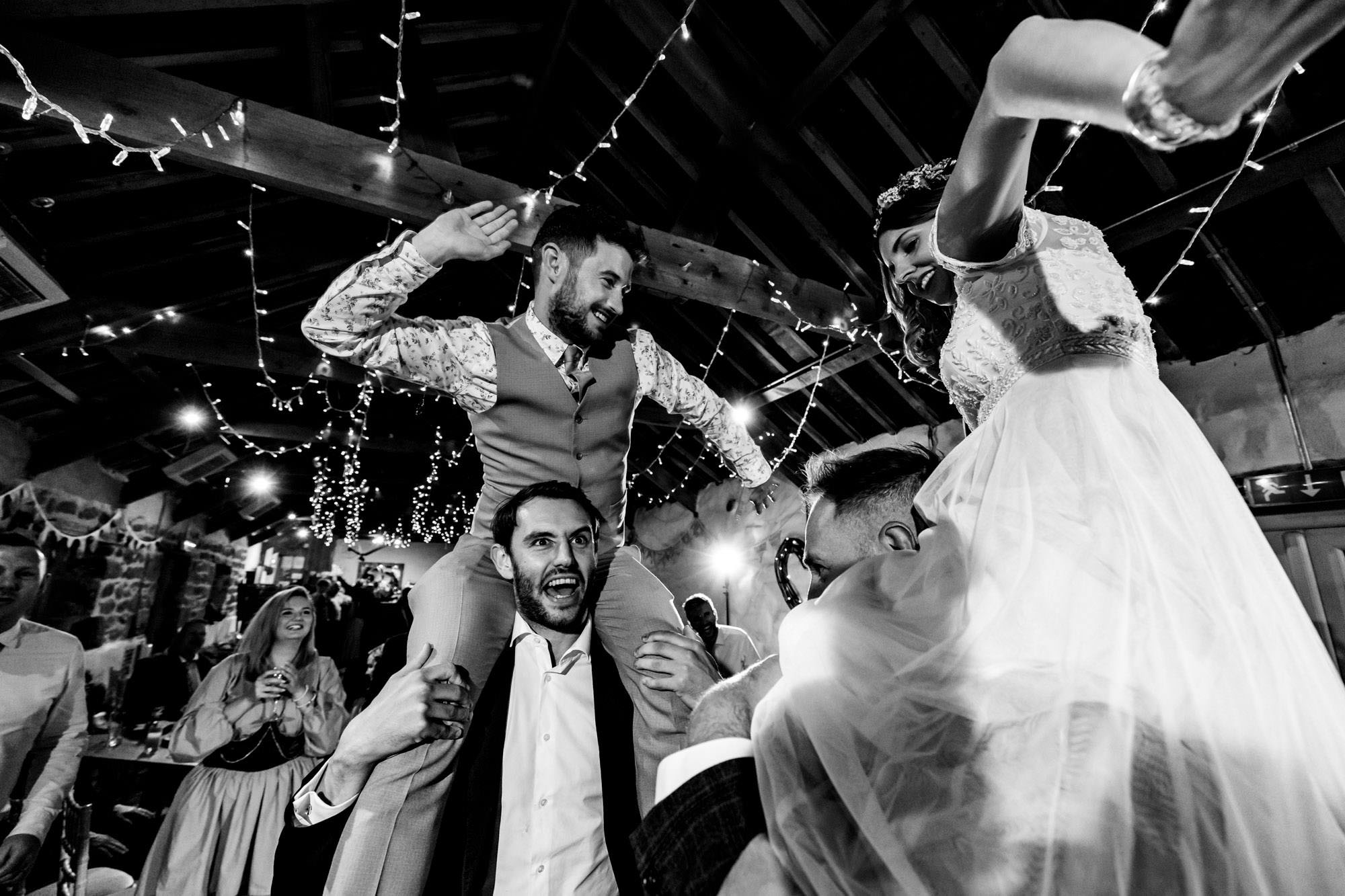 Groom and bride having piggybacks on the dance floor from guests! He's grinning and they're both dancing up there. By Chris Armstrong Photography in Cornwall