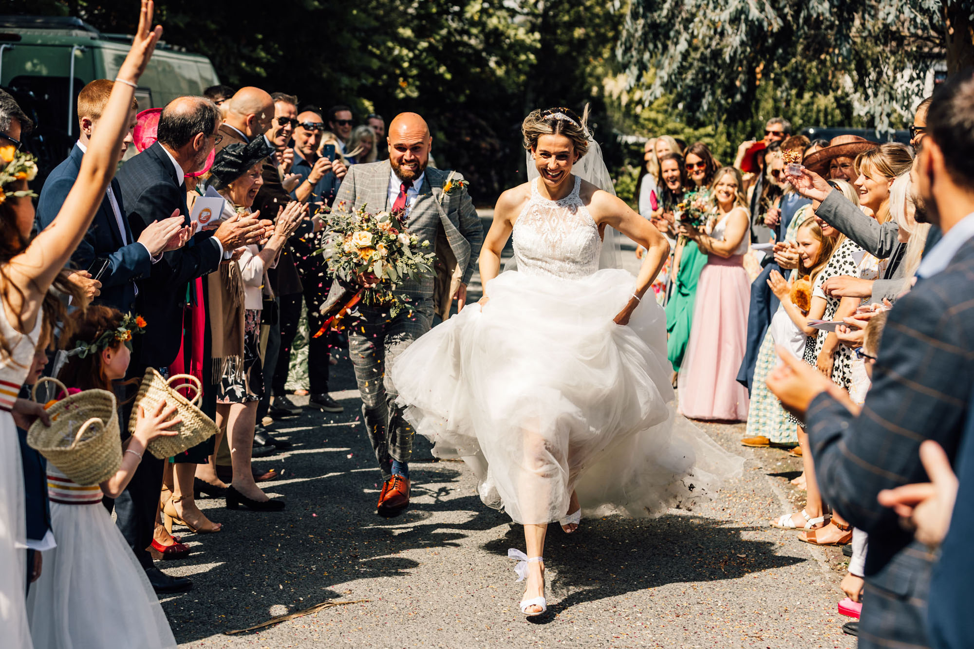Newlyweds running through the confetti throwers! She's hoiked her dress up to run, and he's close behind! By Chris Armstrong Photography in Cornwall