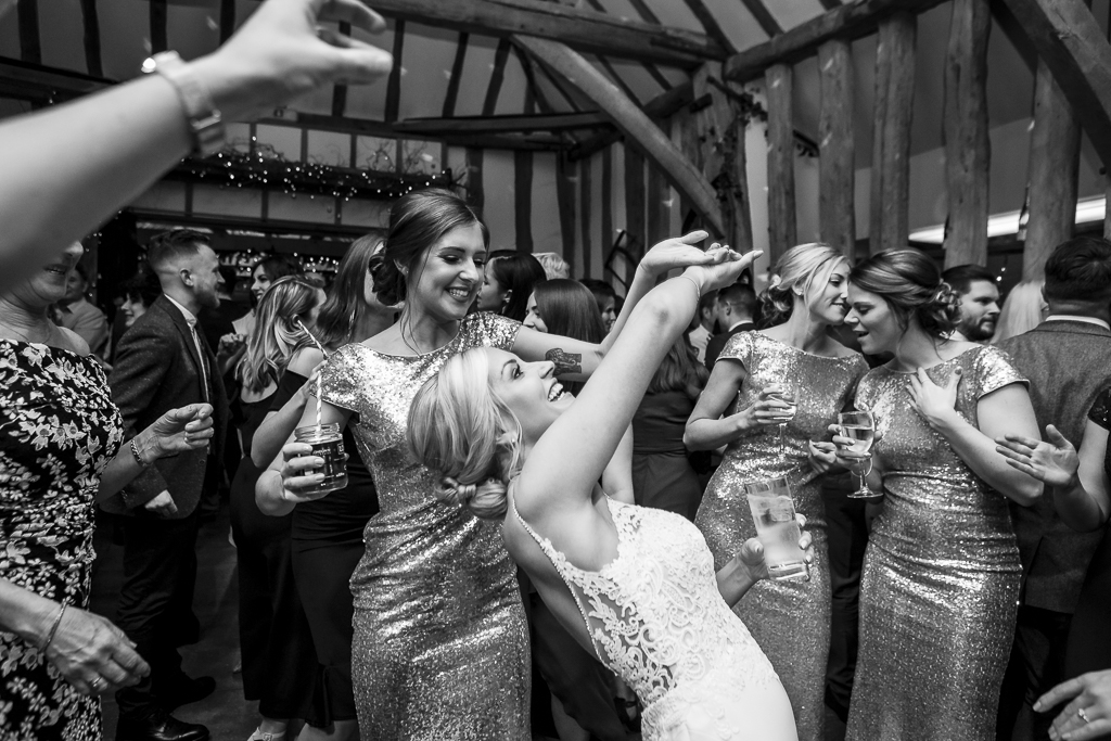 Joyful dance floor photo from a wedding by Ross Willsher Photography. The bride leans back with her arms in the air. One of her bridesmaids is dancing with her, and two more are chatting to the right side of the photo. By Essex wedding photographer Ross Willsher