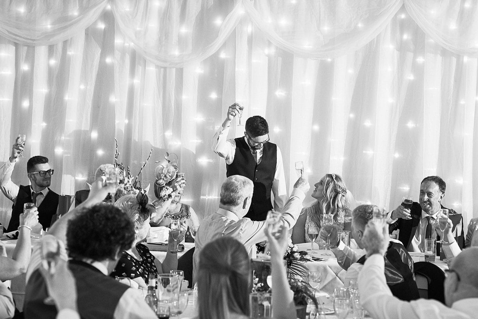 The groom looks down at his bride during the speeches. Black and white photo by 166 Photography