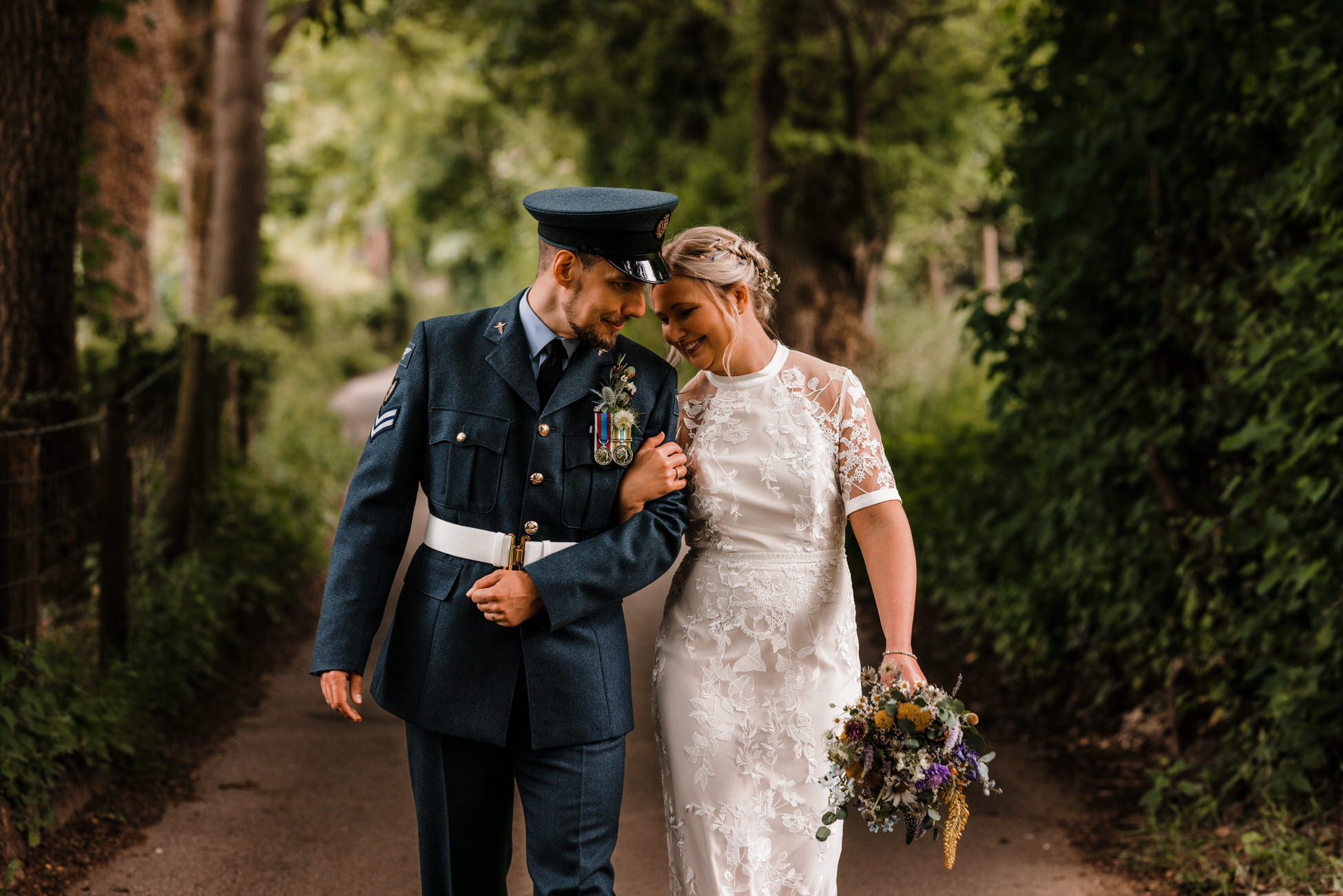 Josh and Lizzy just after their wedding ceremony strolling arm in arm. He's in military uniform and she's carrying a bouquet. By Tom Hodgson Photography