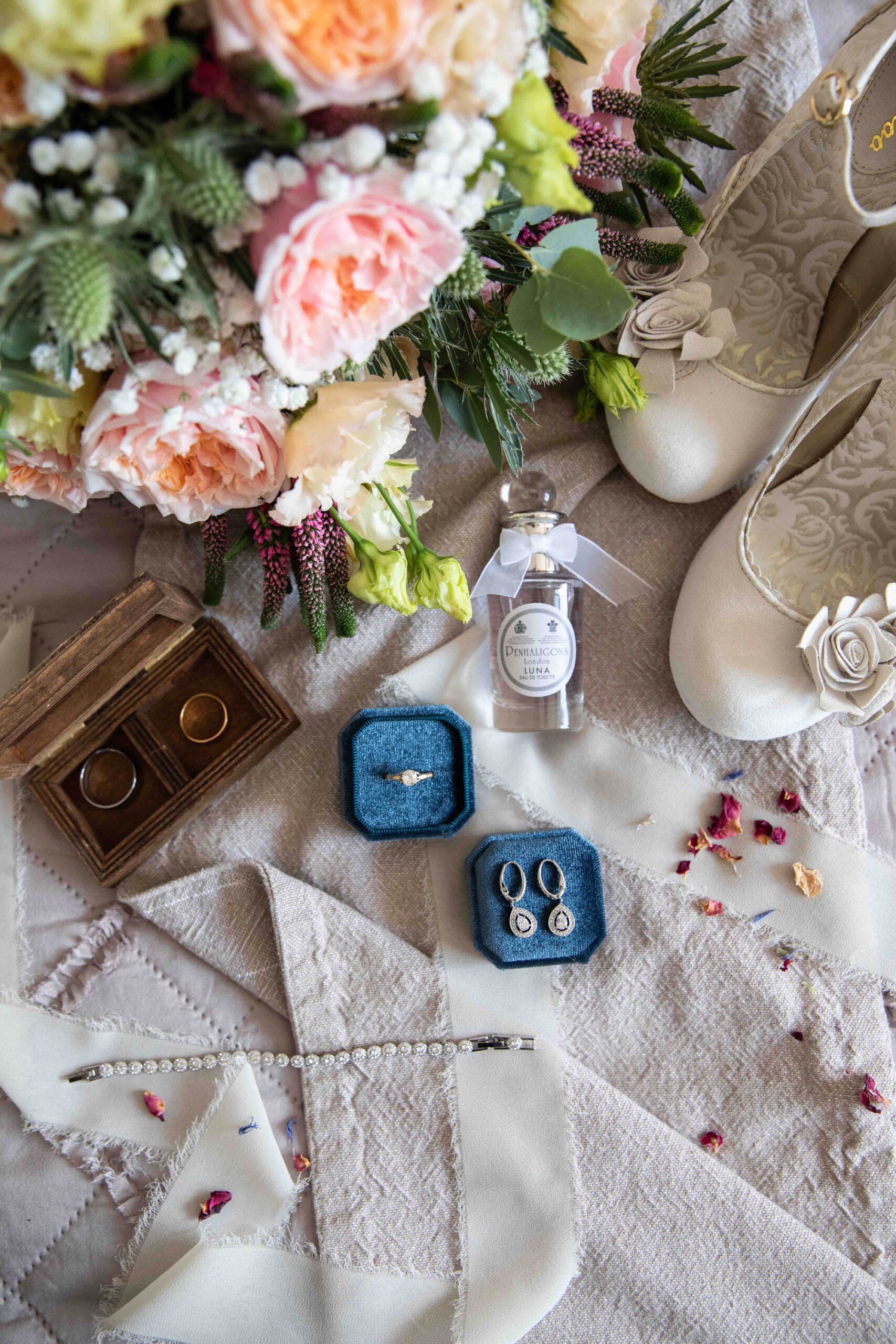 Pretty wedding flatlay image with jewellery in a vintage blue ring box, pale pink roses and white shoes. By Snapdragon Photography in Devon