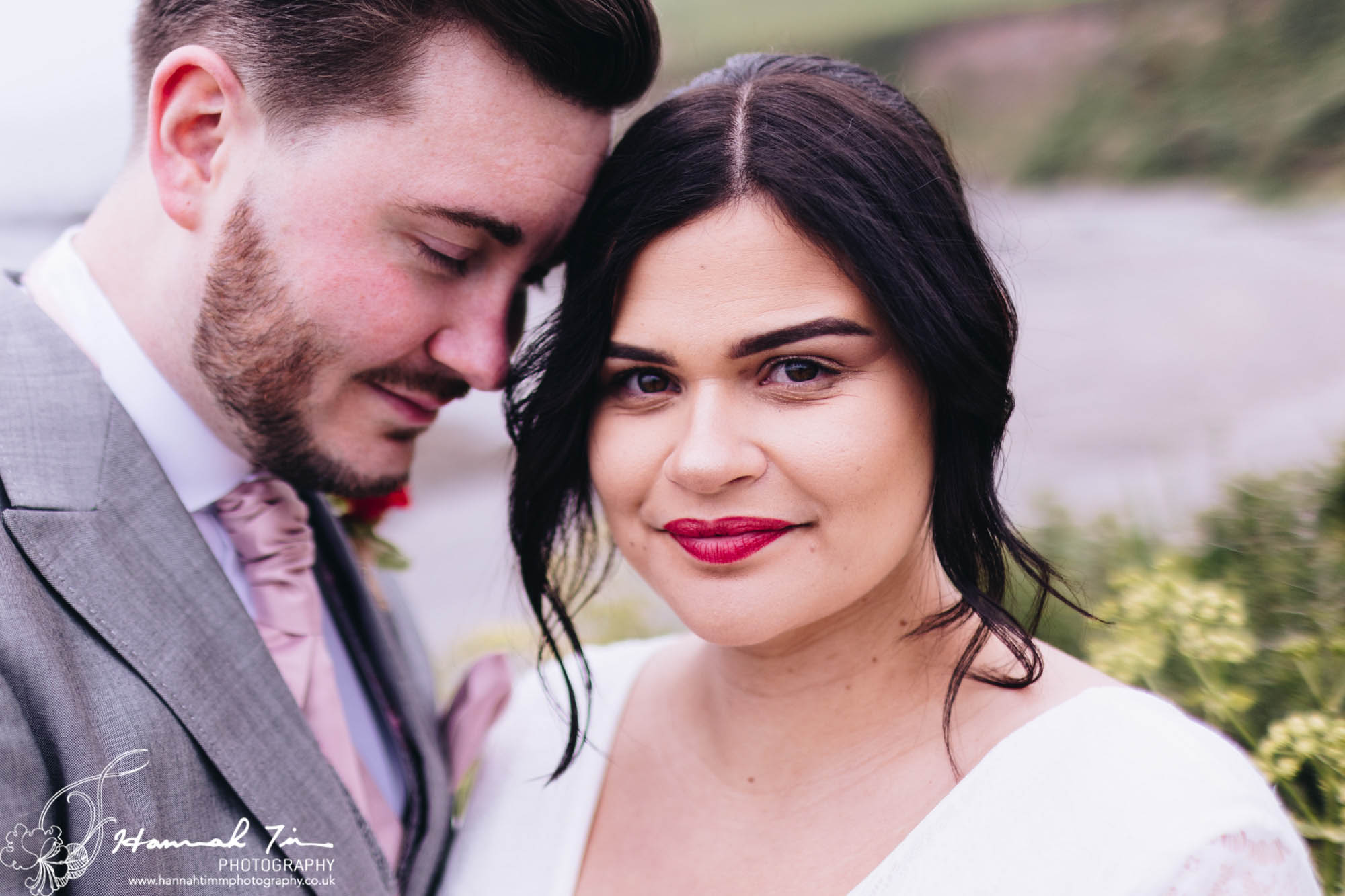 Elopment photography in Cornwall - a bride looks into the camera while her husband rests his head on hers. Close up wedding photography in Cornwall by Hannah Timm