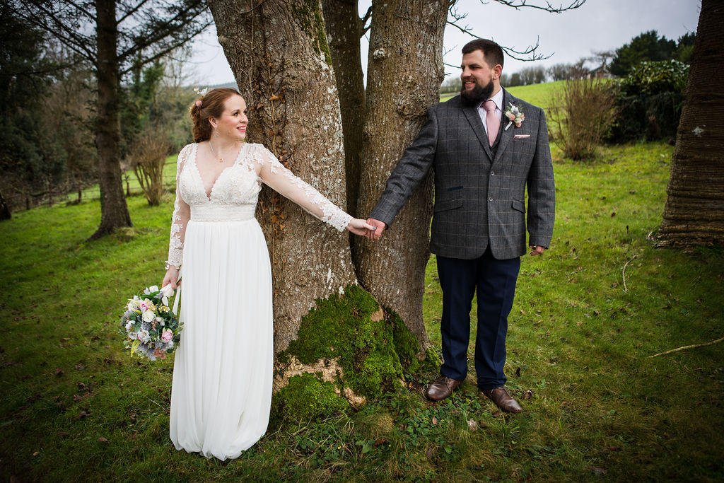 Bride and groom holding hands by a tree at Little Silver Weddings in Devon