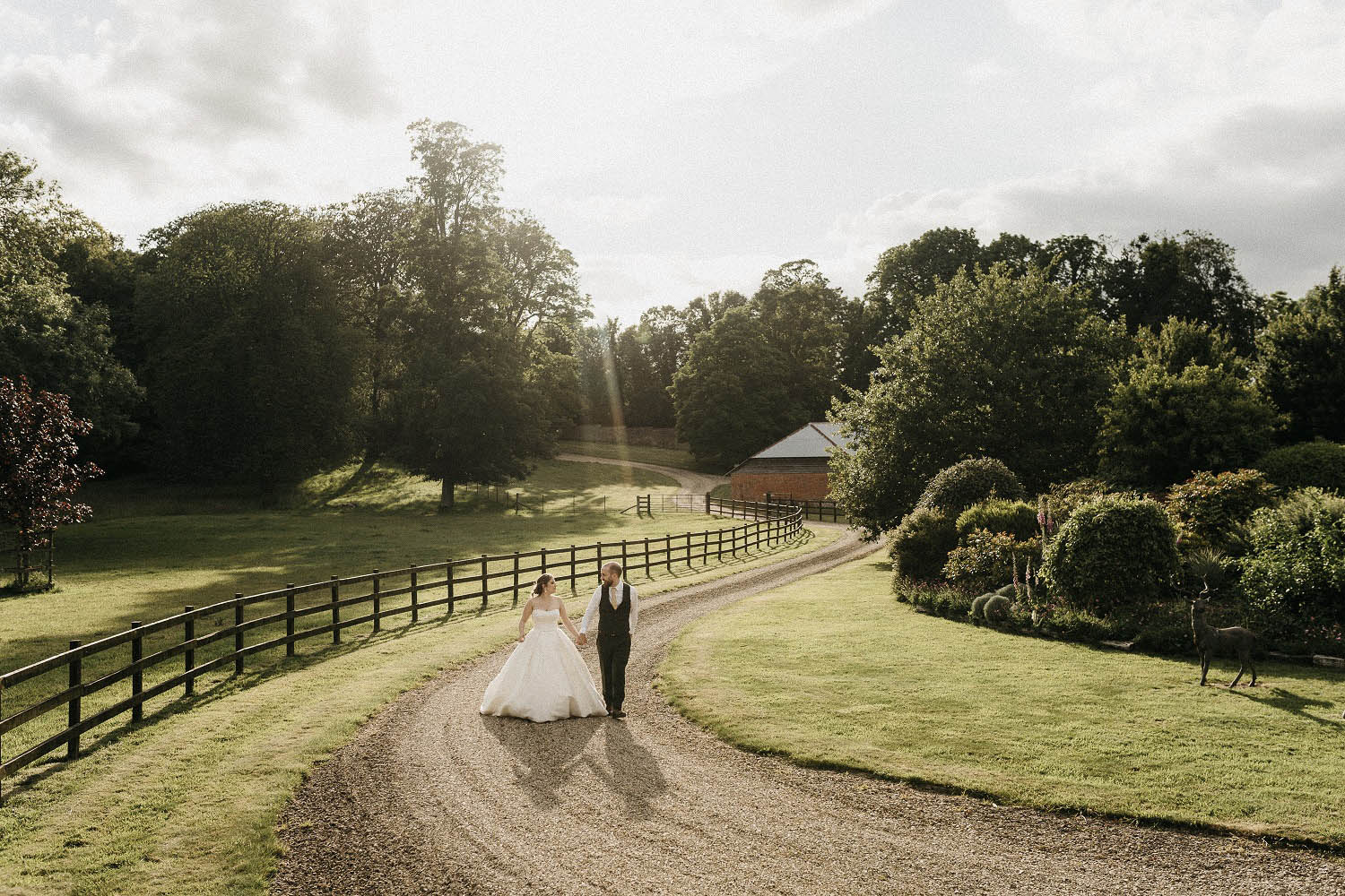 A bride and groom walk down a curving driveway at The Manor Estate Wiltshire