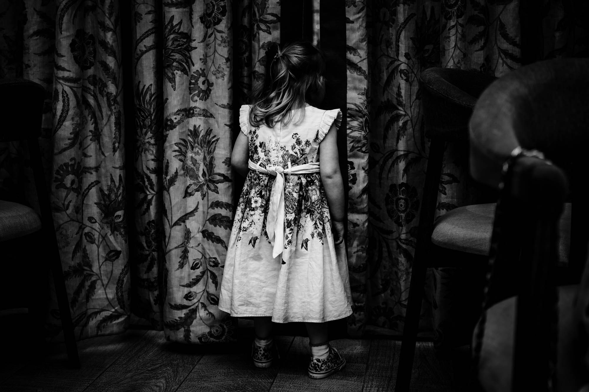 Black and white photo of a little girl in a bridesmaids dress. She's facing away from the camera