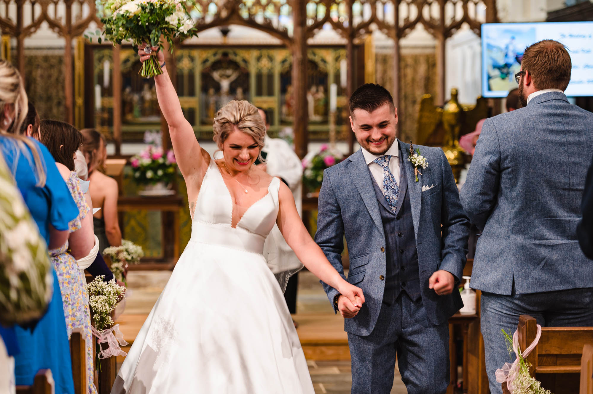 A bride raises her bouquet in the air in celebration as she walks back down the aisle with her husband