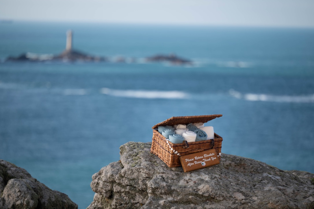 Basket of blankets on a rock with the sea and a lighthouse in the background