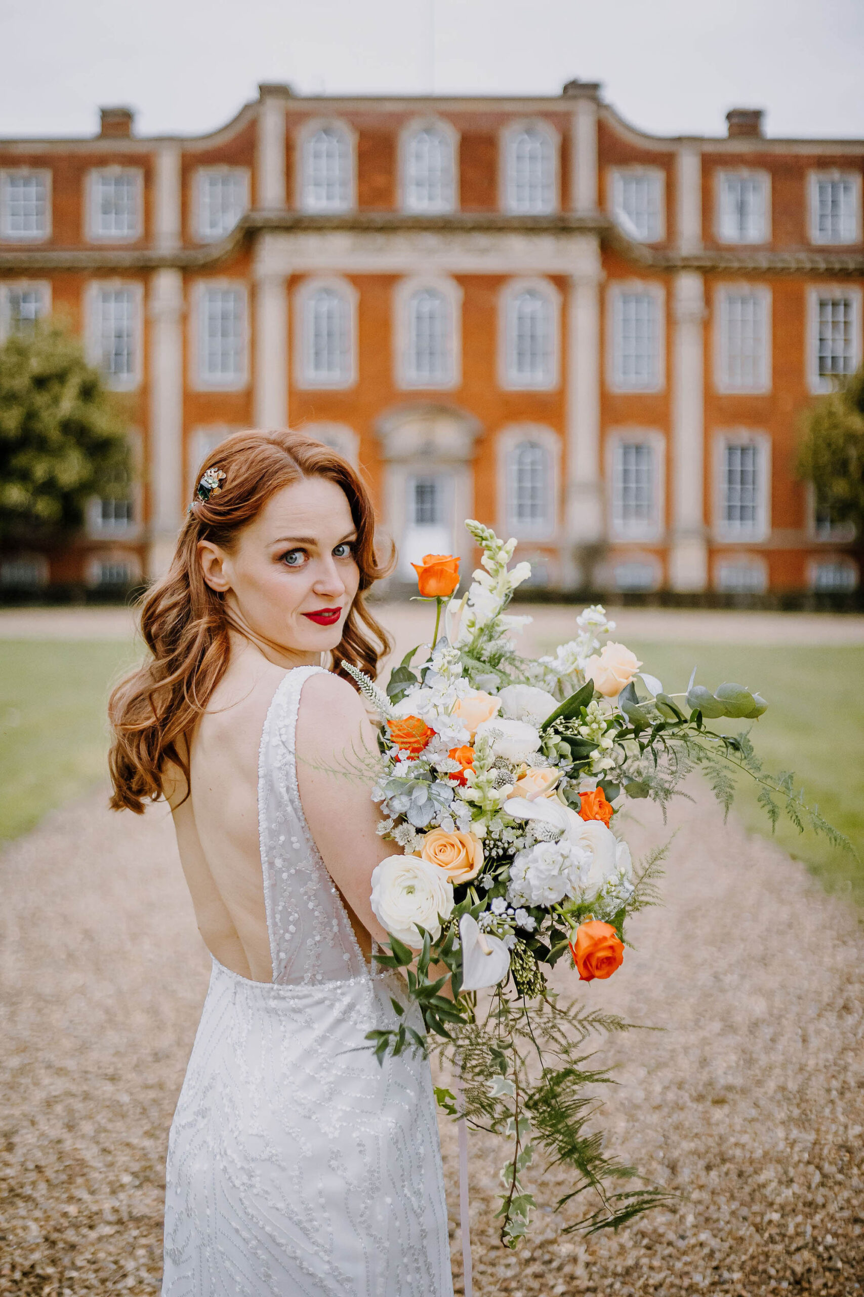 A model in a bridal dress holds a bouquet of white, peach and coral coloured flowers