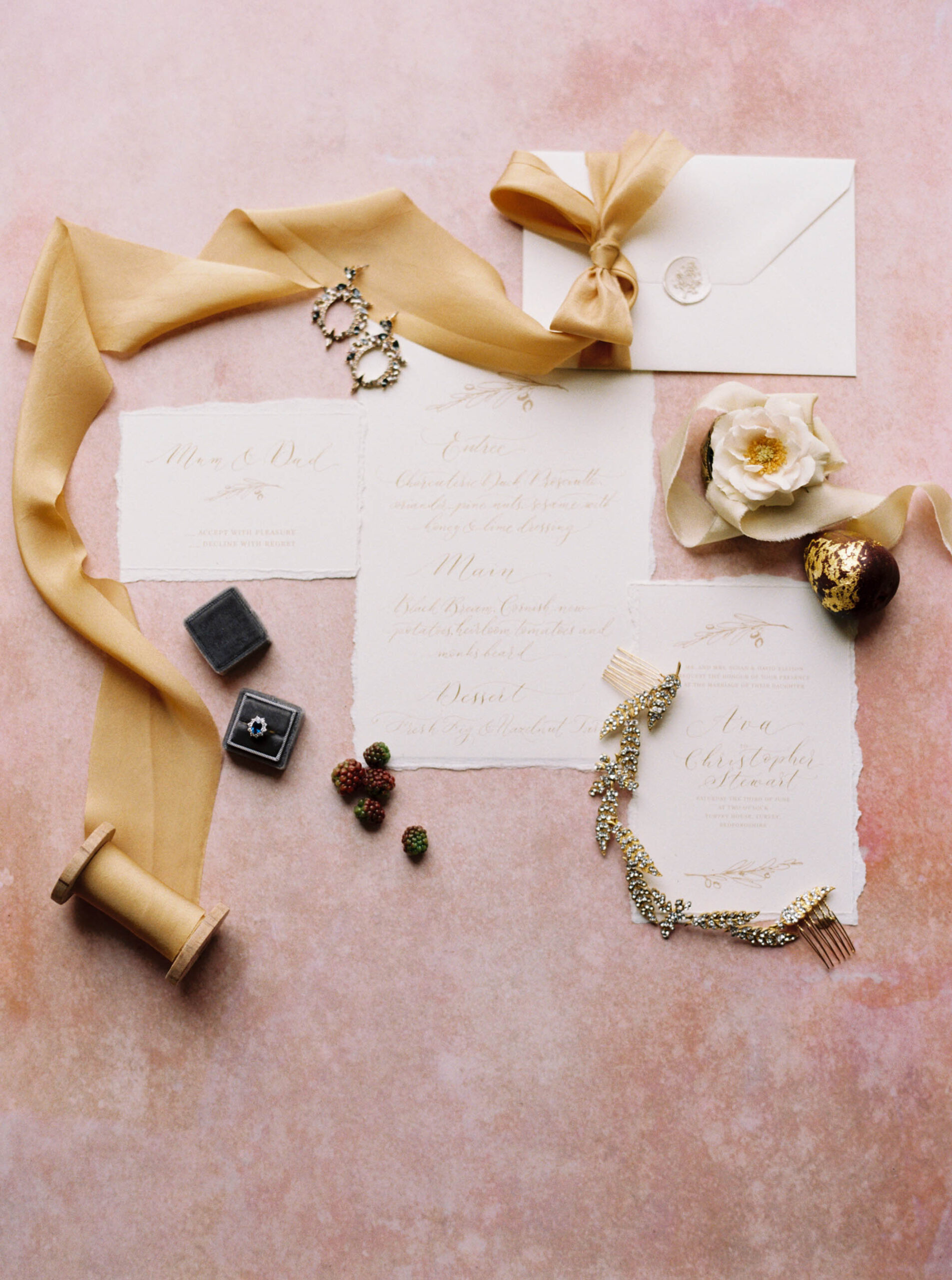 Wedding stationery flatlay with gold calligraphy and silk ribbon.