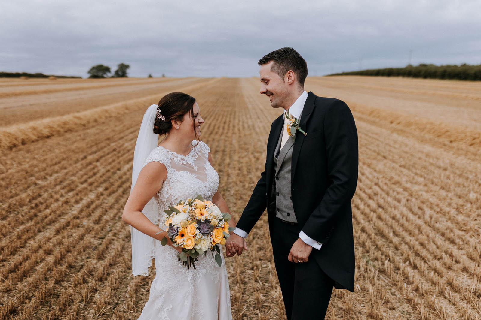 Bride and groom holding hands on a freshly mown hayfield