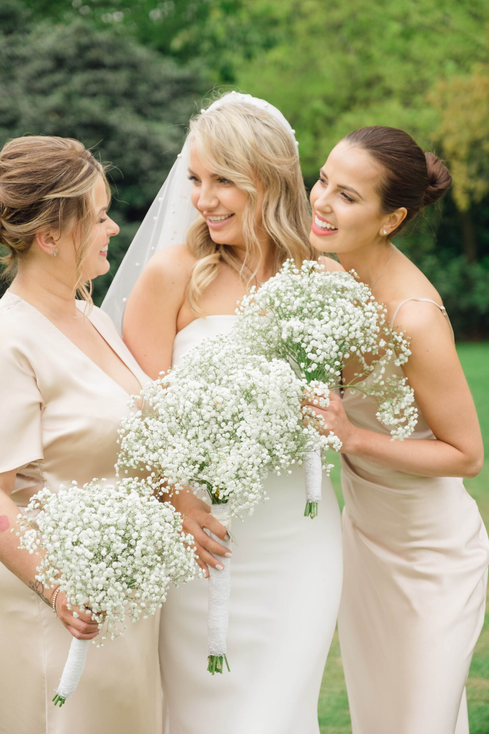 Bride and bridesmaids all with gypsophila bouquets. They're giggling and talking. By Jordan Fox Photography