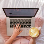 a woman sits cross legged with a laptop and a coffee