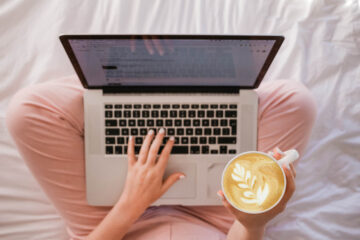 a woman sits cross legged with a laptop and a coffee