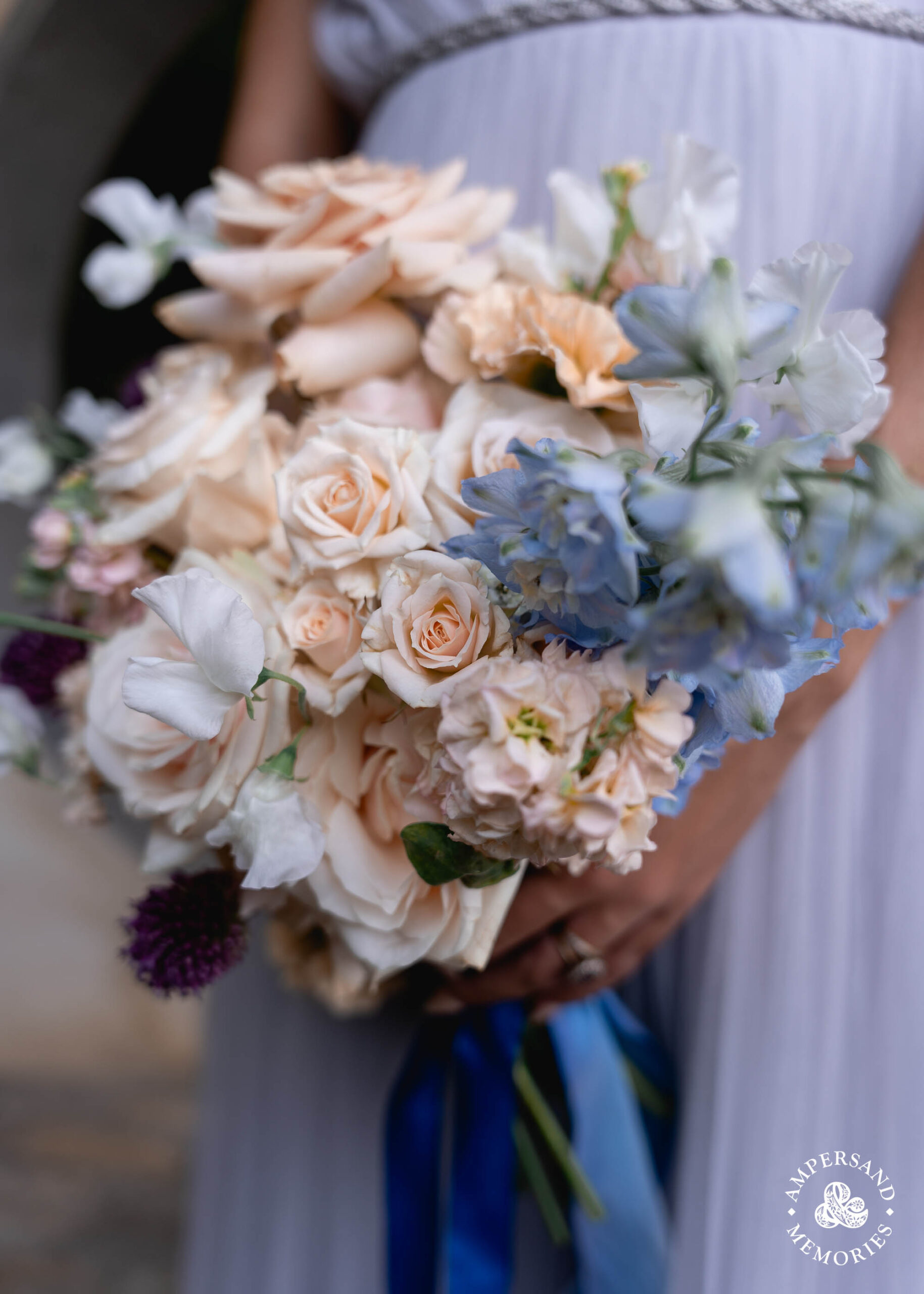 A peach bouquet with blue delphiniums and a blue ribbon