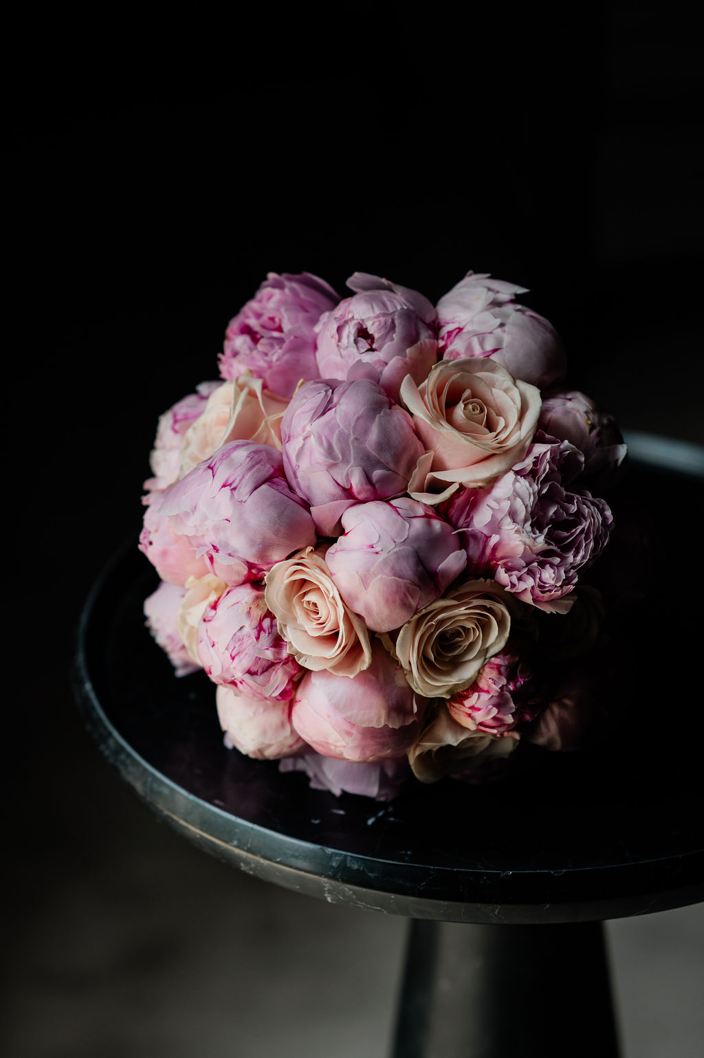Peony and rose bouquet on a dark table with a black background