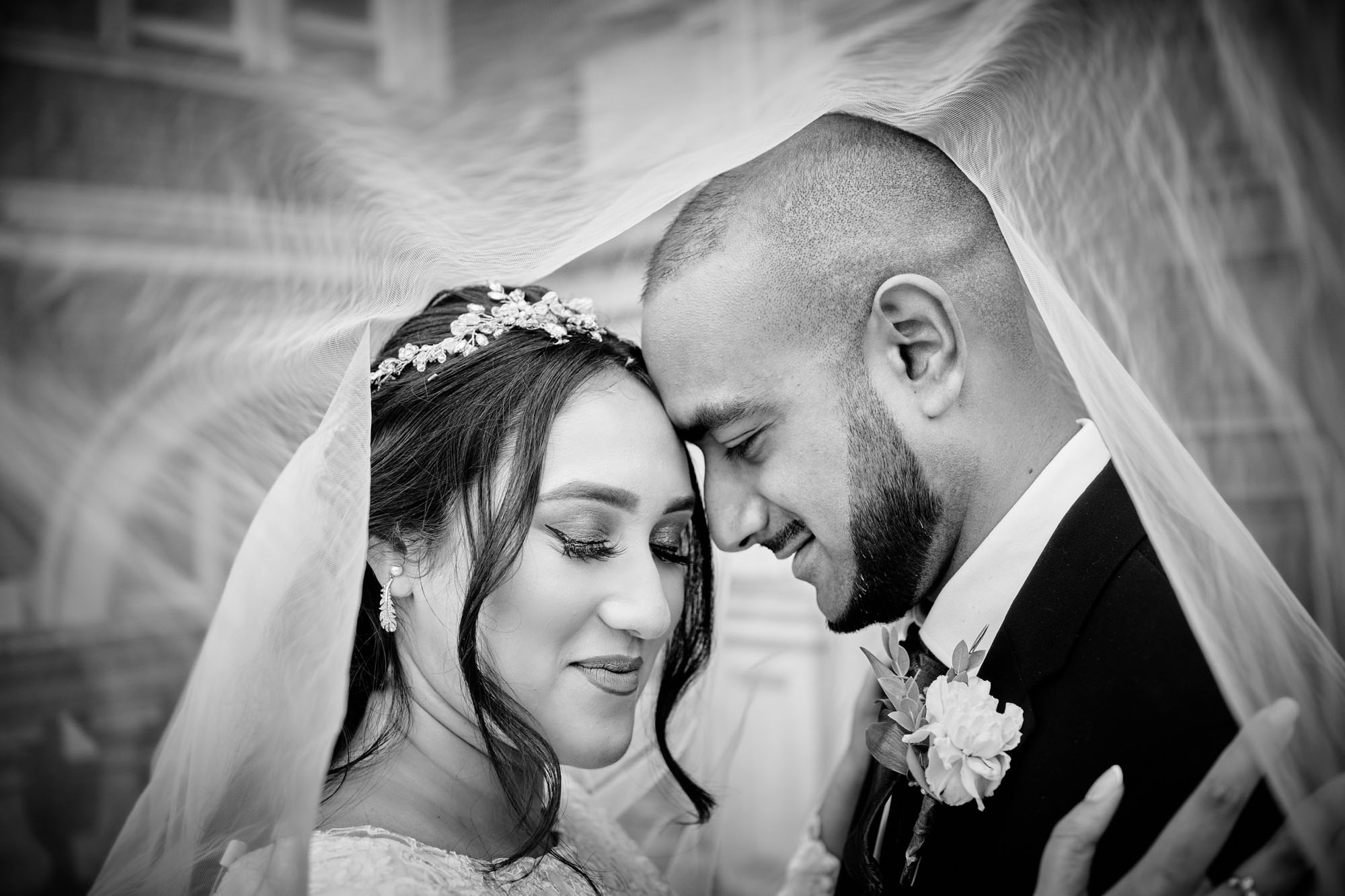 A couple photographed in black and white from beneath the wedding veil. By Howling Basset Photography