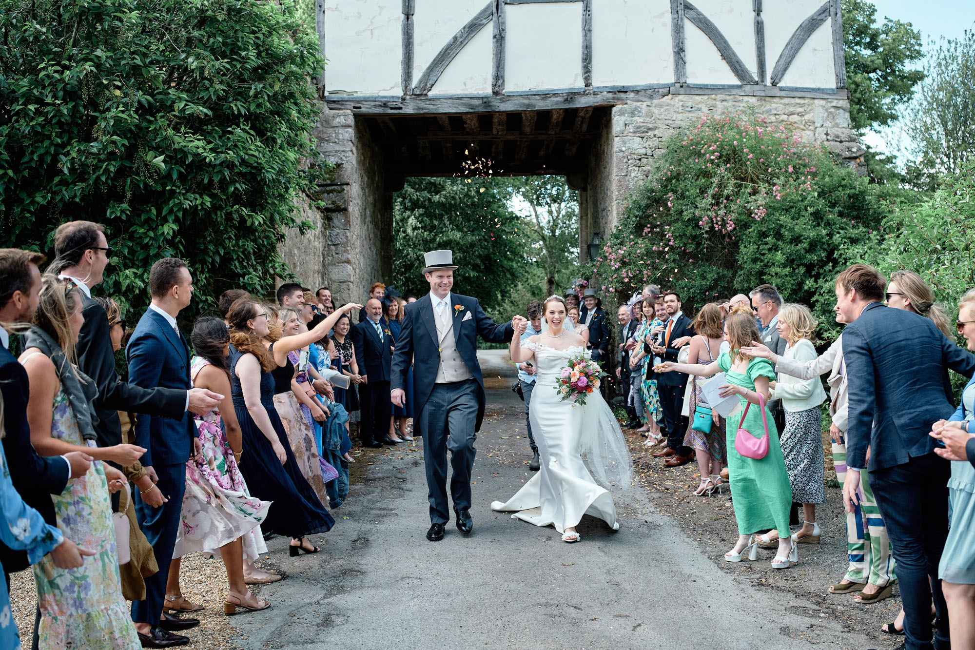 Newlyweds walking between their guests as confetti is thrown. By Howling Basset Photography