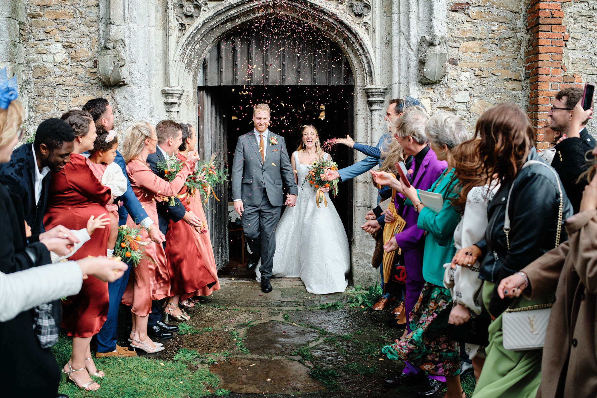 Groom and bride leaving the wedding as guests throw confetti. By Howling Bassett Photography