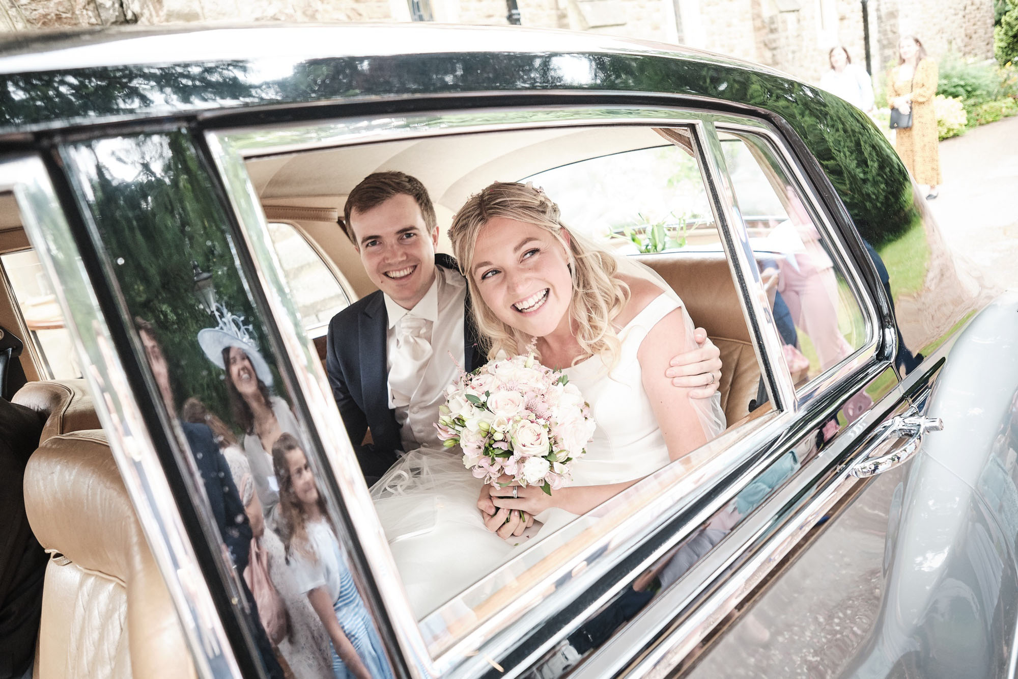 Couple in the back of their wedding car, by Howling Basset Photography