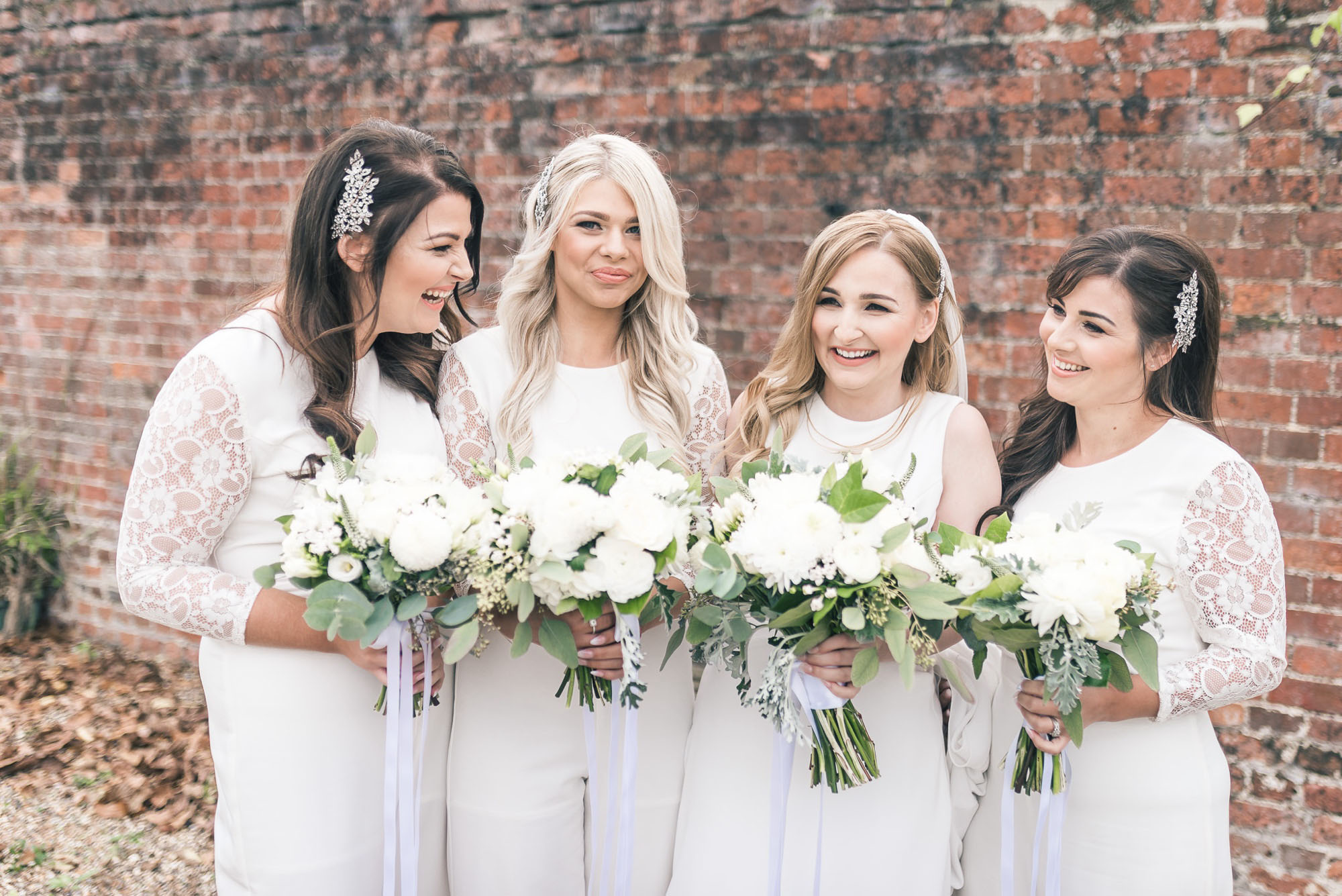 Bridesmaids holding white bouquets with green foliage. By Howling Basset Photography