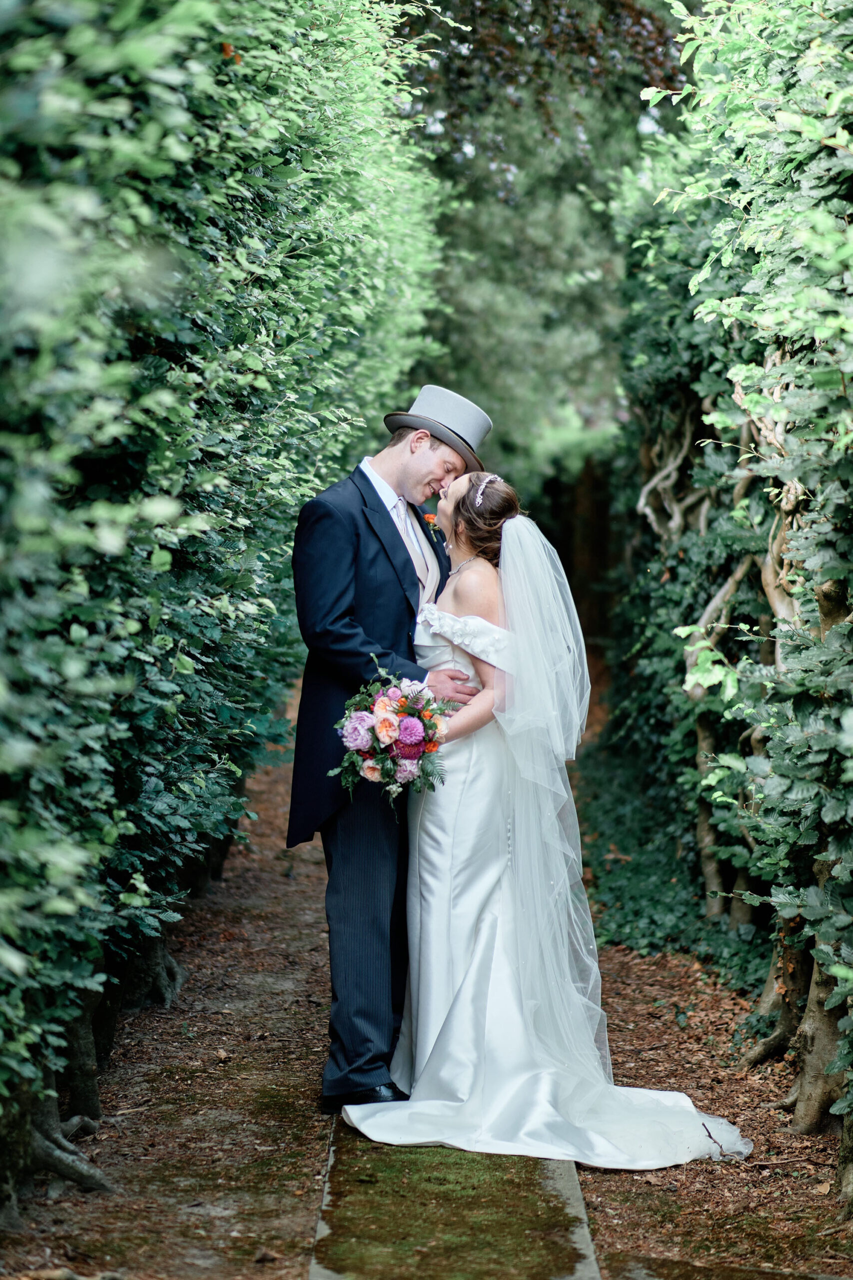 Wedding portrait of a couple kissing in a leafy landscaped garden. By Howling Basset Photography in Kent