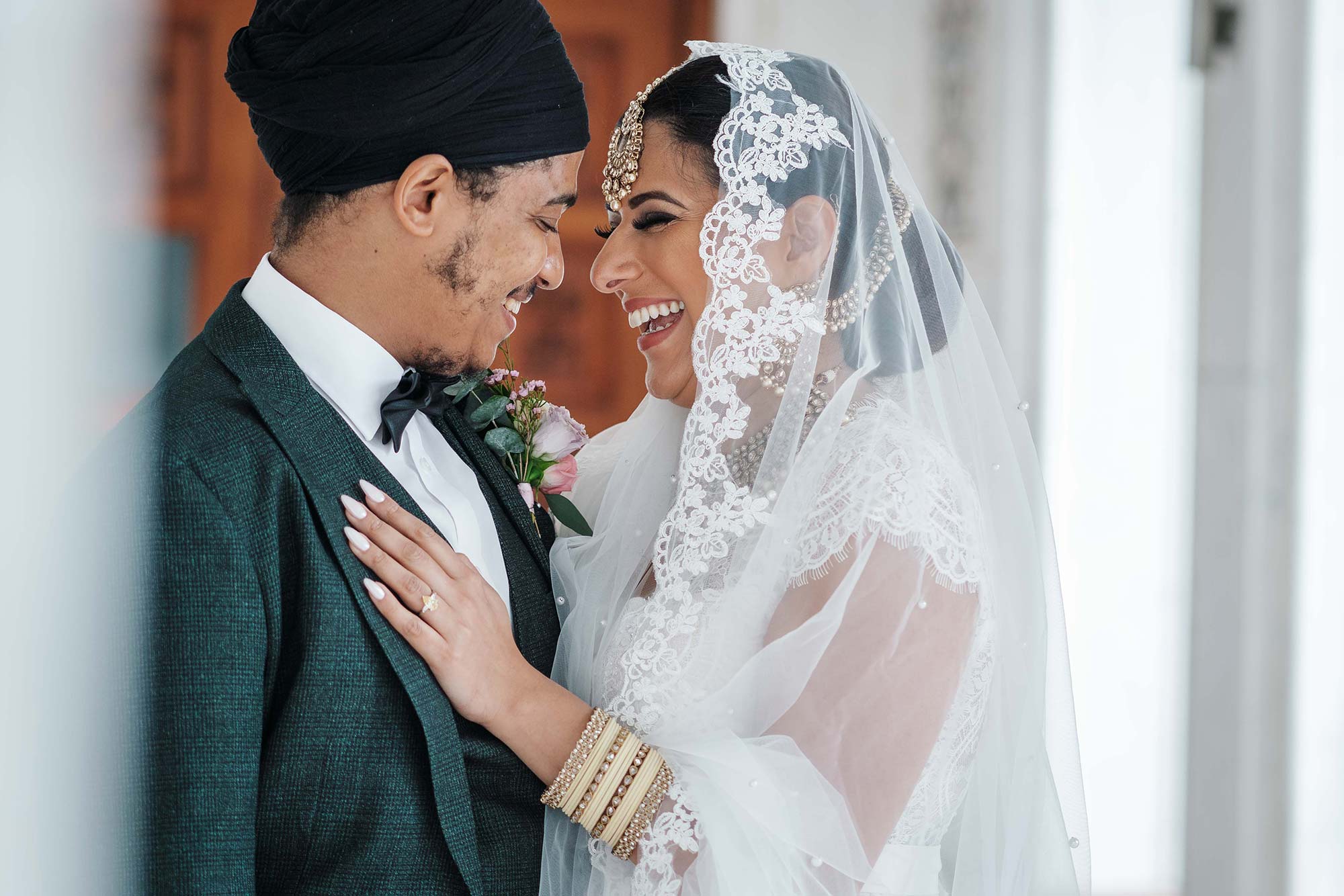 Groom and bride laughing and hugging. She's wearing a veil and has her hand on his chest. By Dorset wedding photographers Smiling Tiger Studios