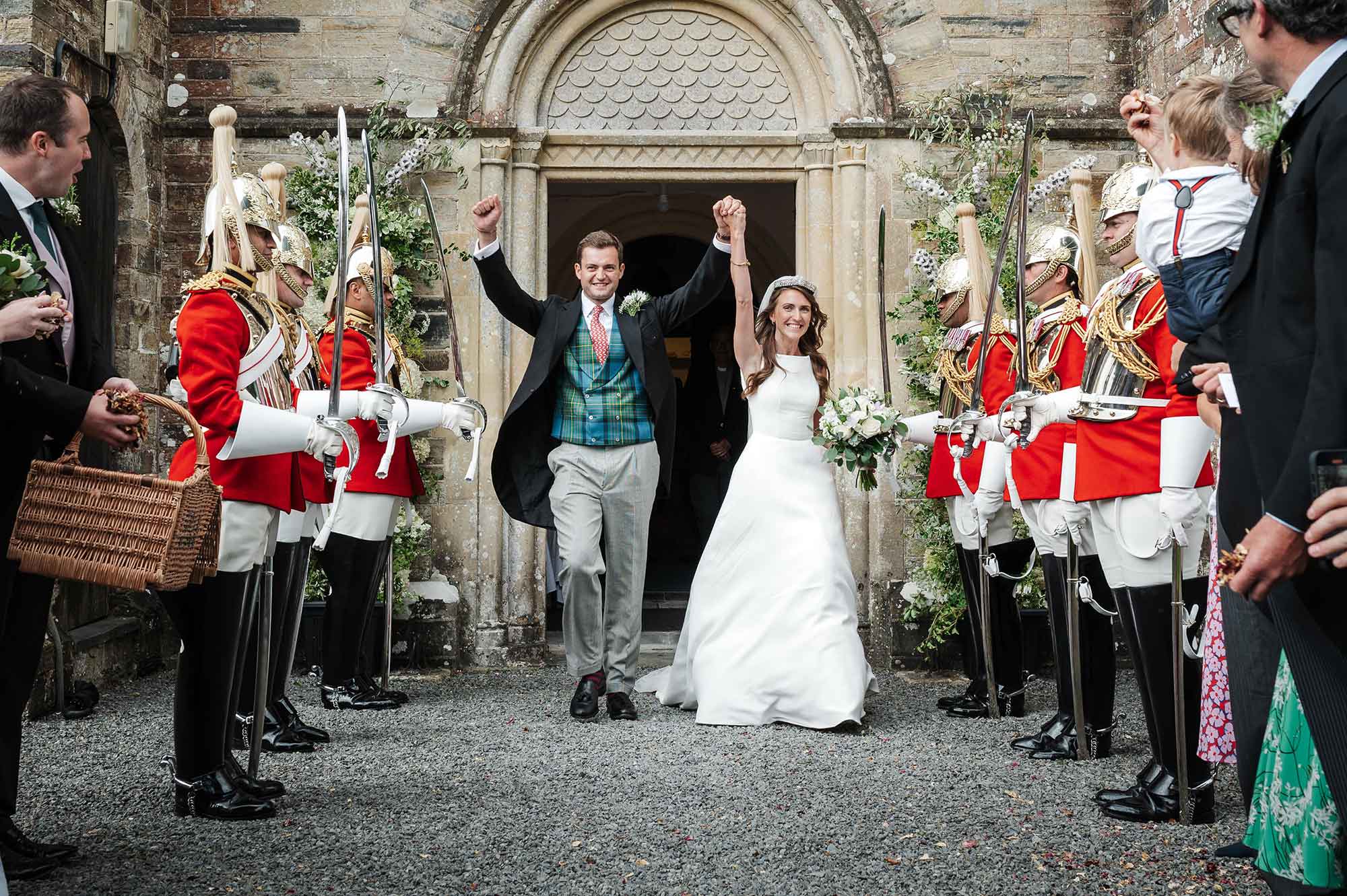 Newlywed couple with raised hands coming out of the church and through a military welcome. by Smiling Tiger Studios