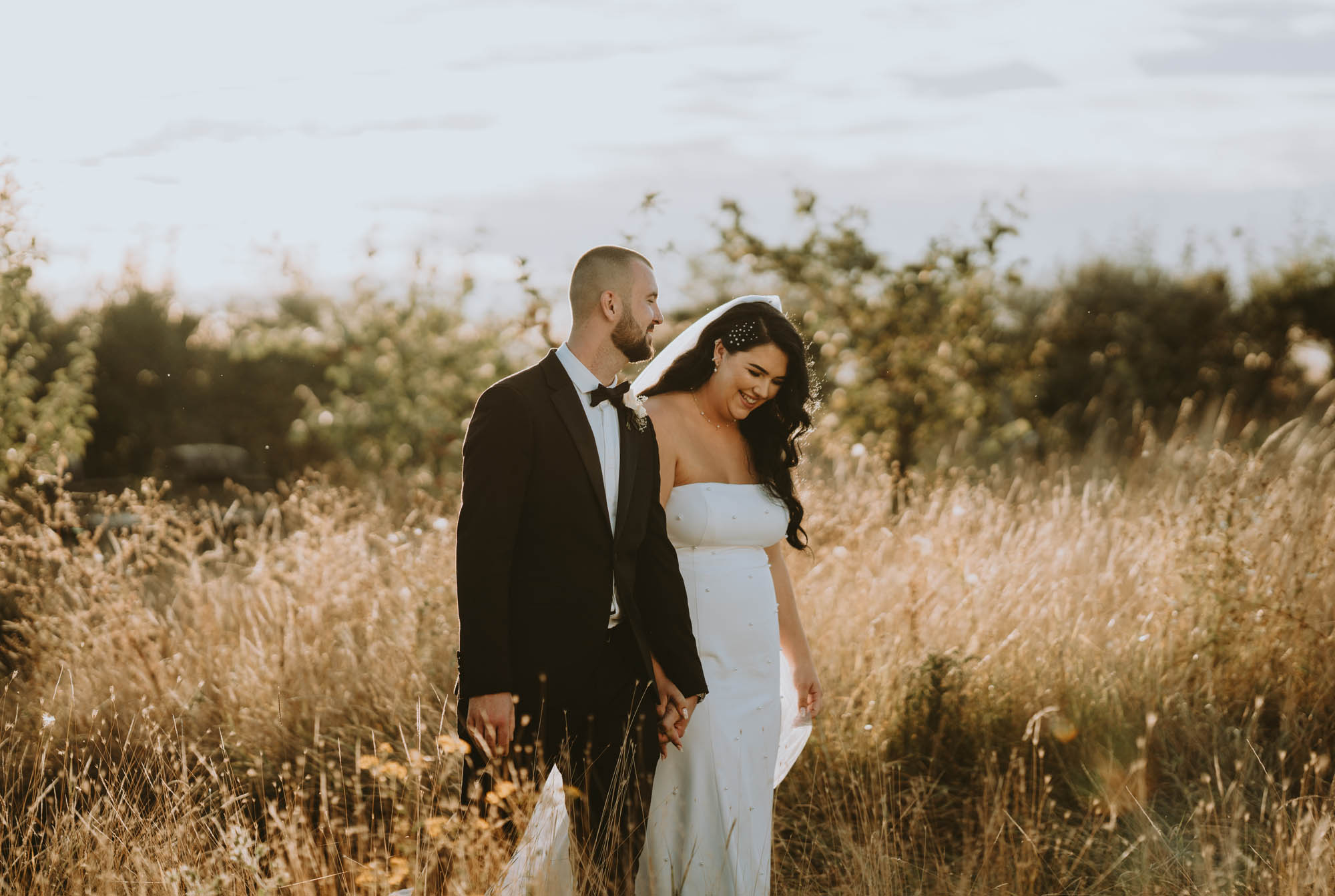 Newlyweds in a corn field. The groom wears black tie and the bride is in a strapless dress with veil. Image by Space Shark Weddings