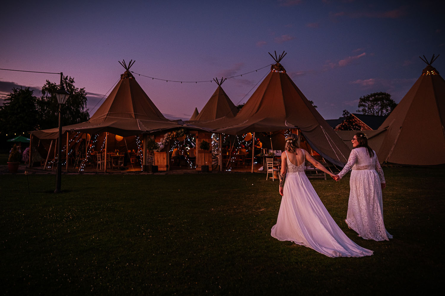 Two brides at sunset, walking towards their tipi wedding hand in hand. Simon Dewey Photography