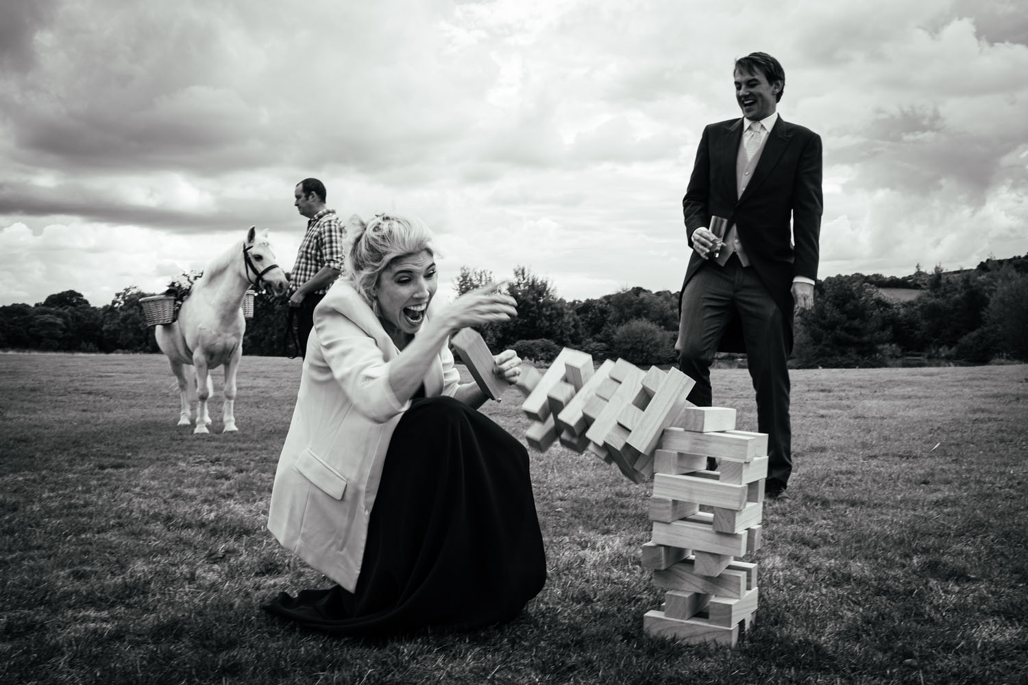 A wedding guest gleefully loses at jenga while a man talks to his pony and another guest laughs. Simon Dewey Photography Derby