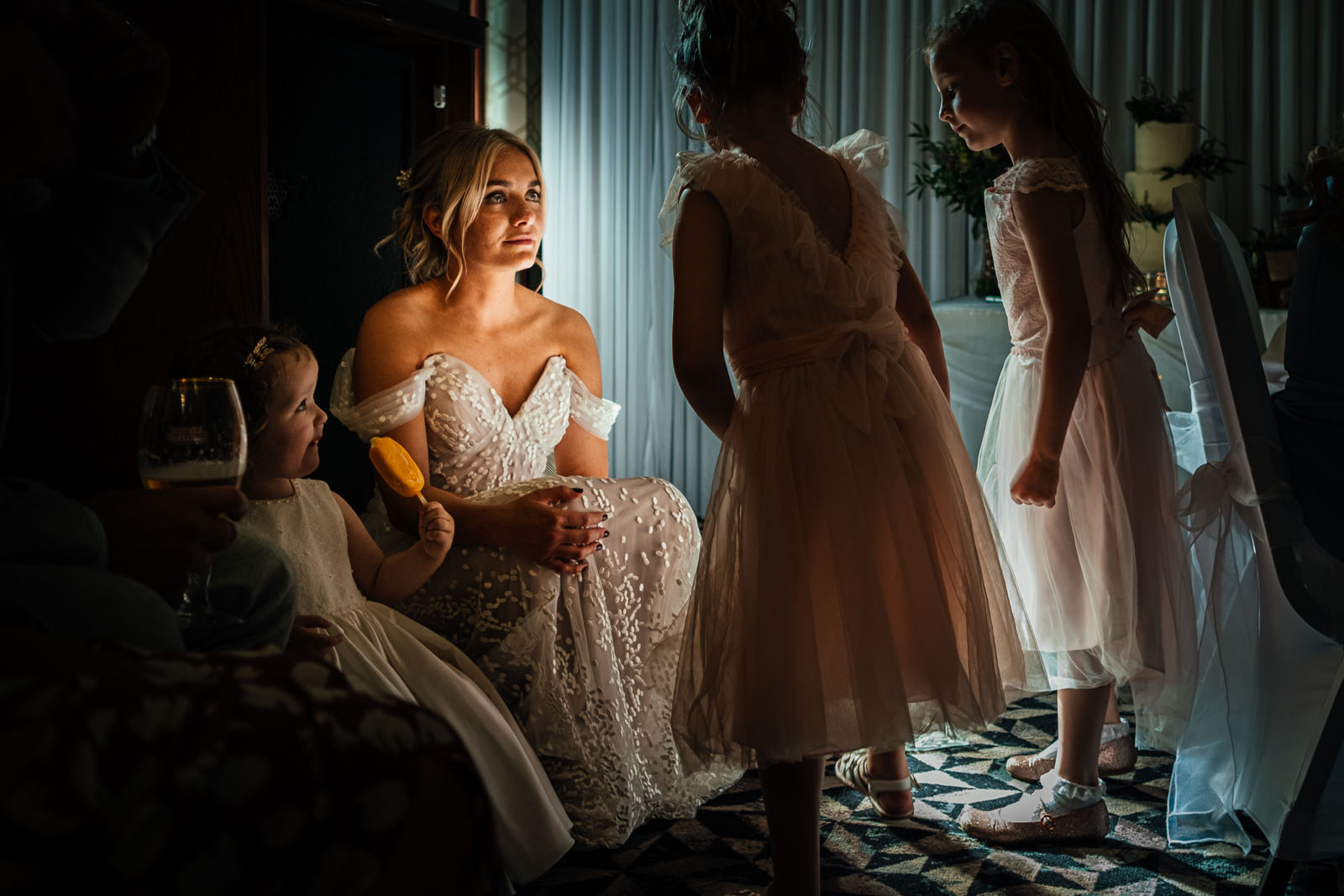 A beautifully lit wedding photograph in documentary style of a bride surrounded by little bridesmaids who are deep in conversation. Taken by Derby wedding photographer Simon Dewey