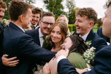 Wedding group hug with groomsmen, bridesmaid and newlyweds. By Libra Photographic Poole Dorset