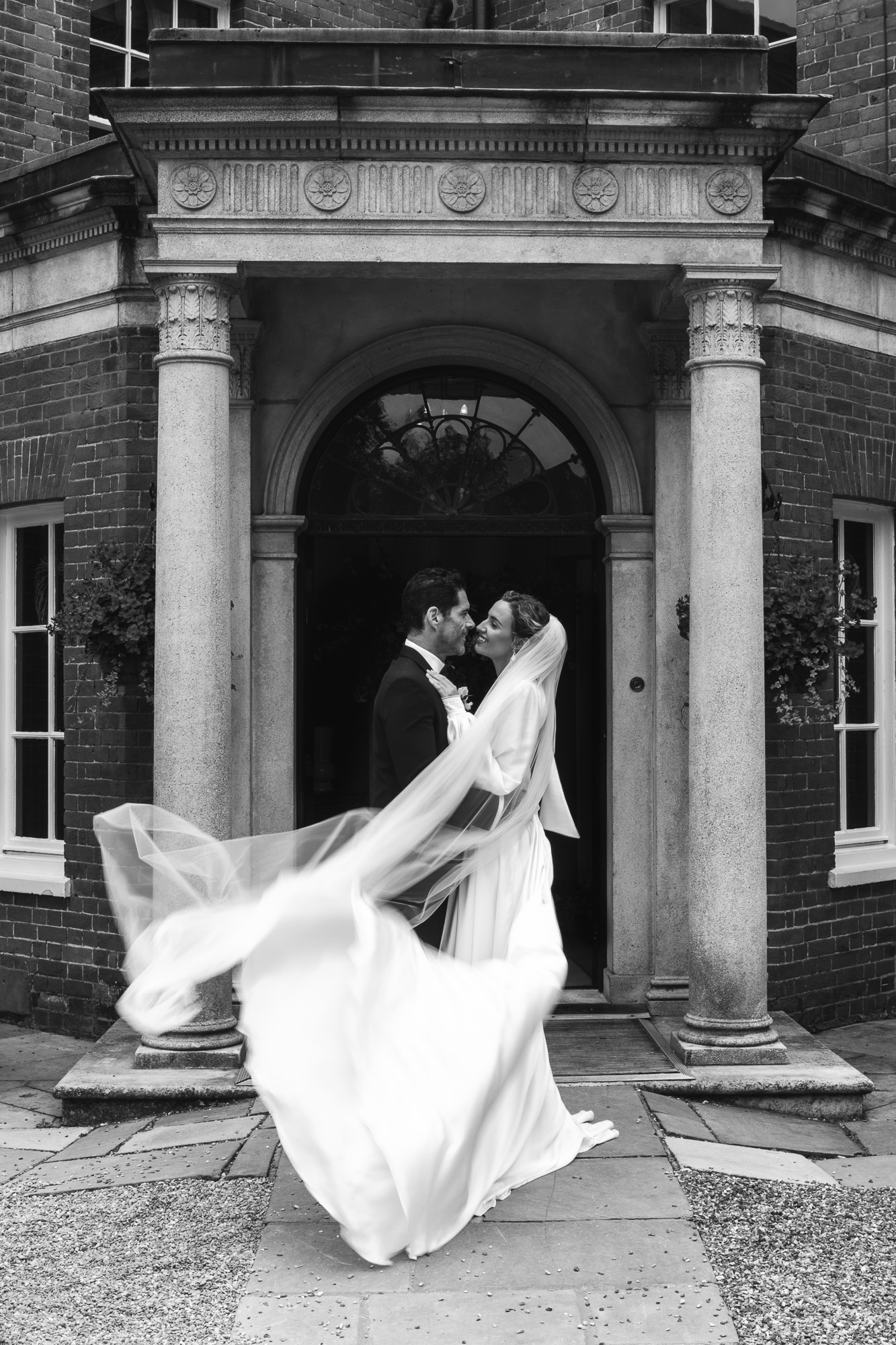 Newlywed couple embracing outside their wedding venue. Black and white photography by Ross Willsher, Essex wedding photographer