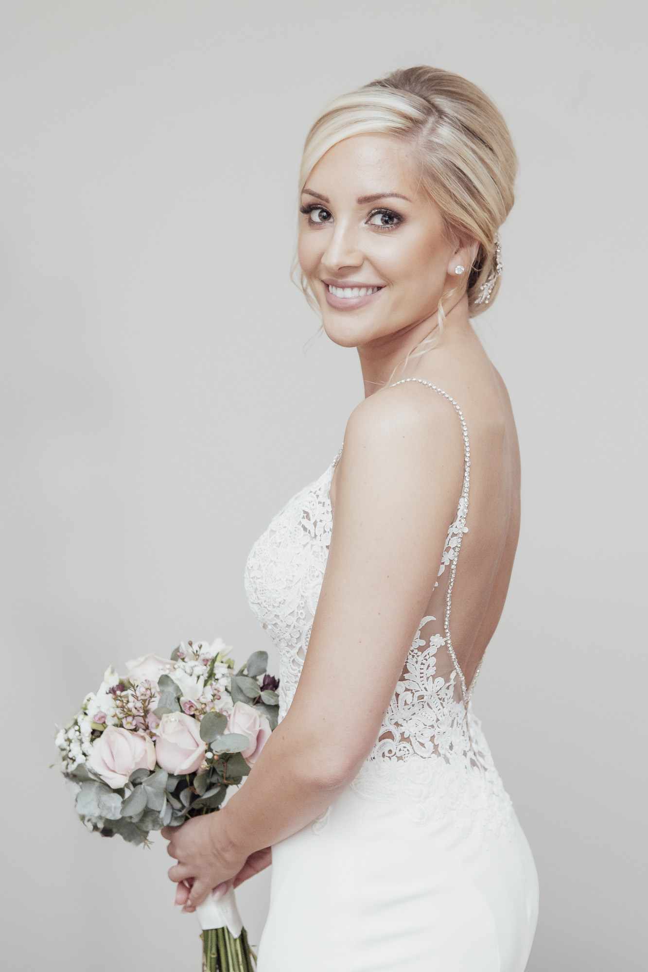 Bride smiling at the camera, holding a pastel bouquet in her hands. By Ross Willsher Photography