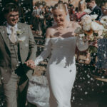 Groom and bride walk hand in hand outside Yorkshire's Thirst Barn as guests throw petal confetti. Photography by Joss Denham