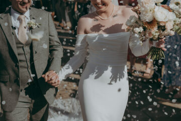 Groom and bride walk hand in hand outside Yorkshire's Thirst Barn as guests throw petal confetti. Photography by Joss Denham