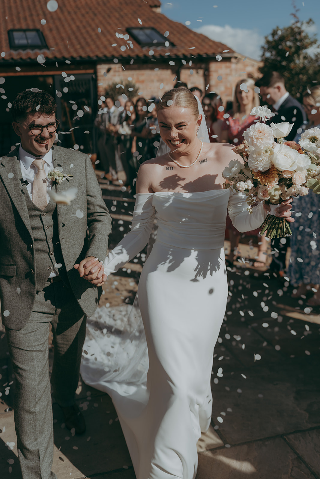 Groom and bride walk hand in hand outside Yorkshire's Thirst Barn as guests throw petal confetti. Photography by Joss Denham