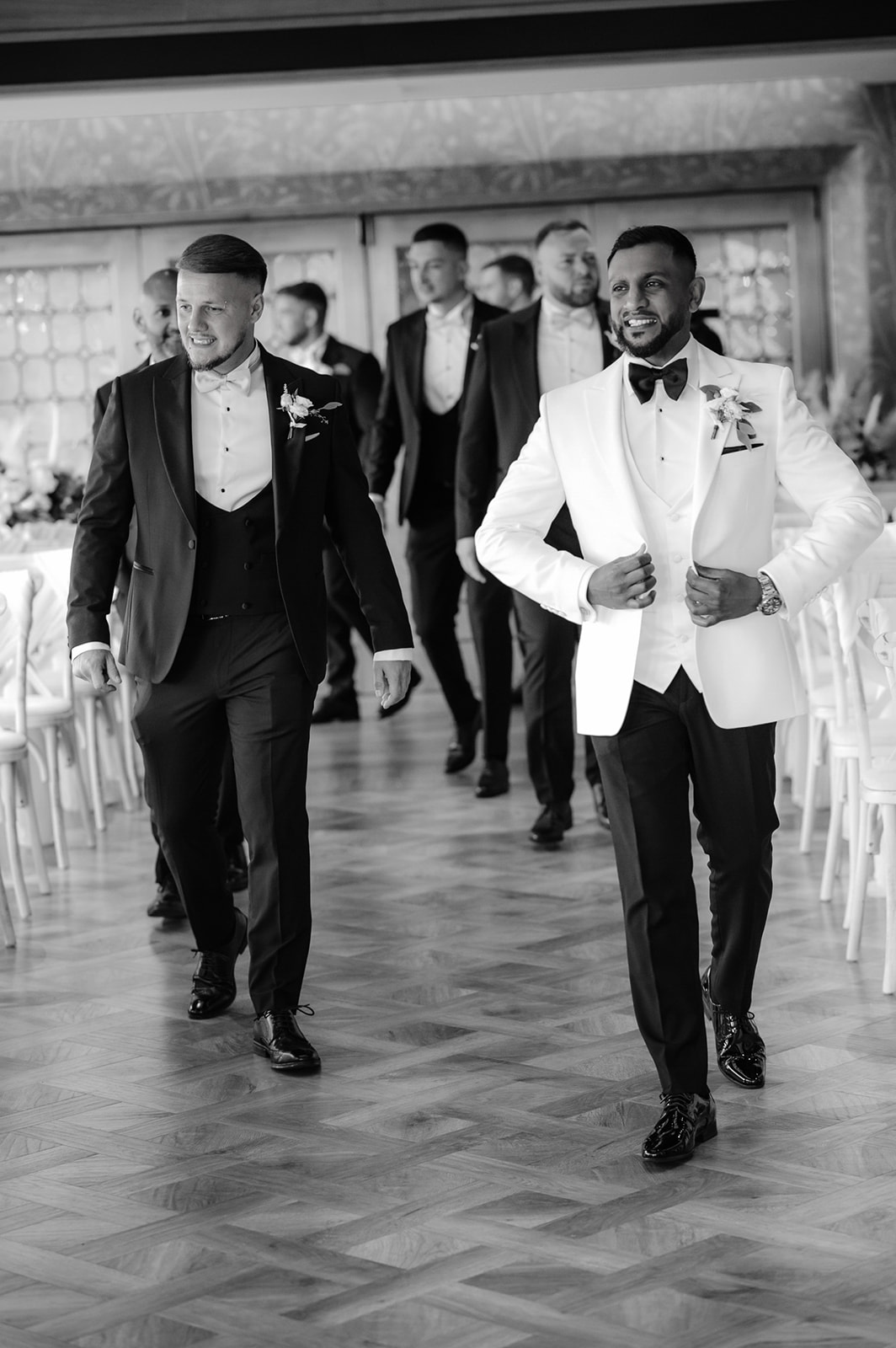 Natural documentary photo from a luxury black tie wedding in Cambridge as the groom and groomsmen walk towards the photographer - Damien Vickers