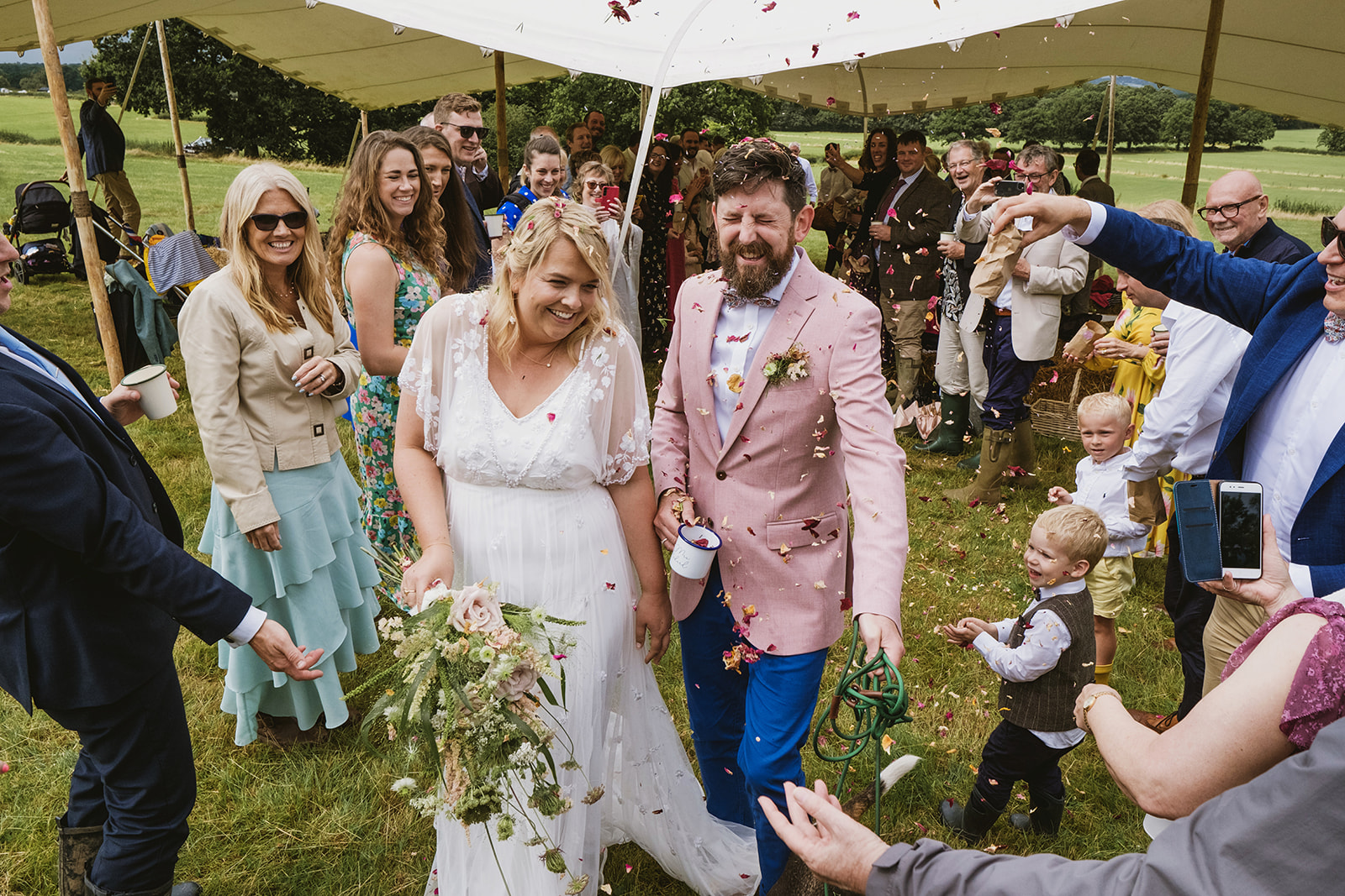 newlyweds laugh as guests throw petal confetti | outdoor wedding in Kent with award winning UK photographers York Place Studios