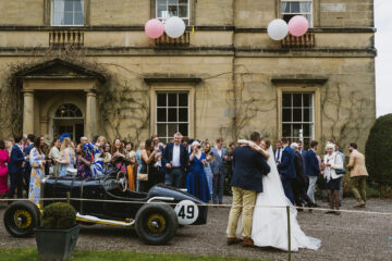 Newlyweds outside Middleton Lodge wedding venue with a vintage car and their guests waiting outside | documentary wedding photography by York Place Studios