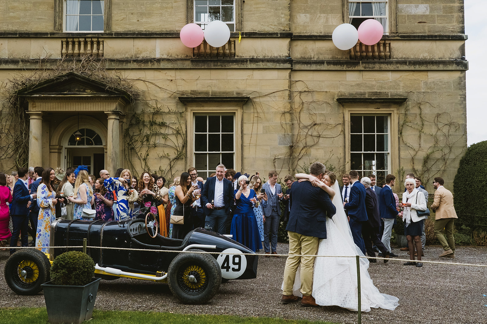 Newlyweds outside Middleton Lodge wedding venue with a vintage car and their guests waiting outside | documentary wedding photography by York Place Studios