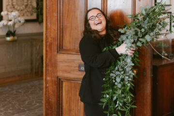 Lauren Batten event planner holding a bundle of foliage and laughing by a wooden door