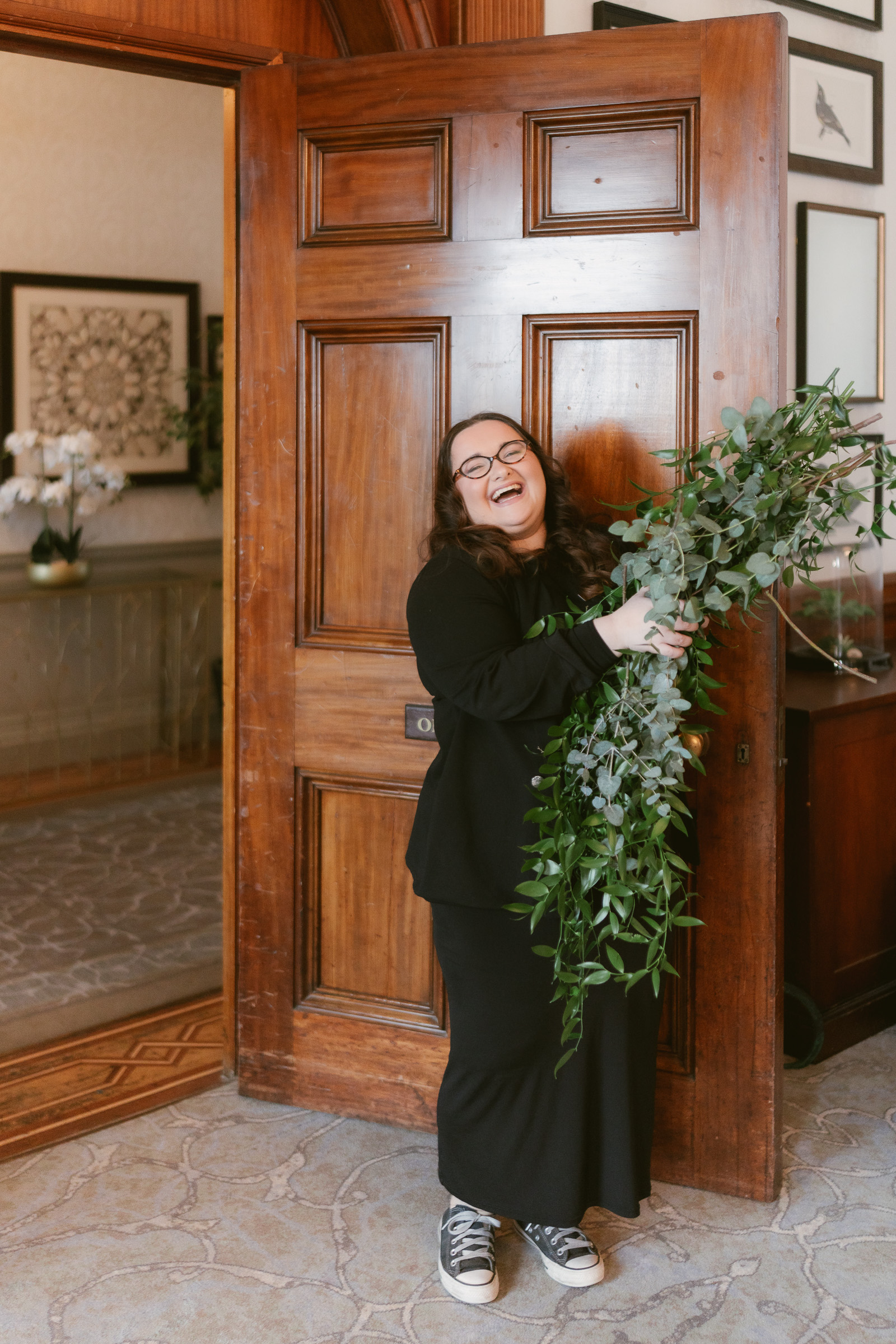 Lauren Batten event planner holding a bundle of foliage and laughing by a wooden door