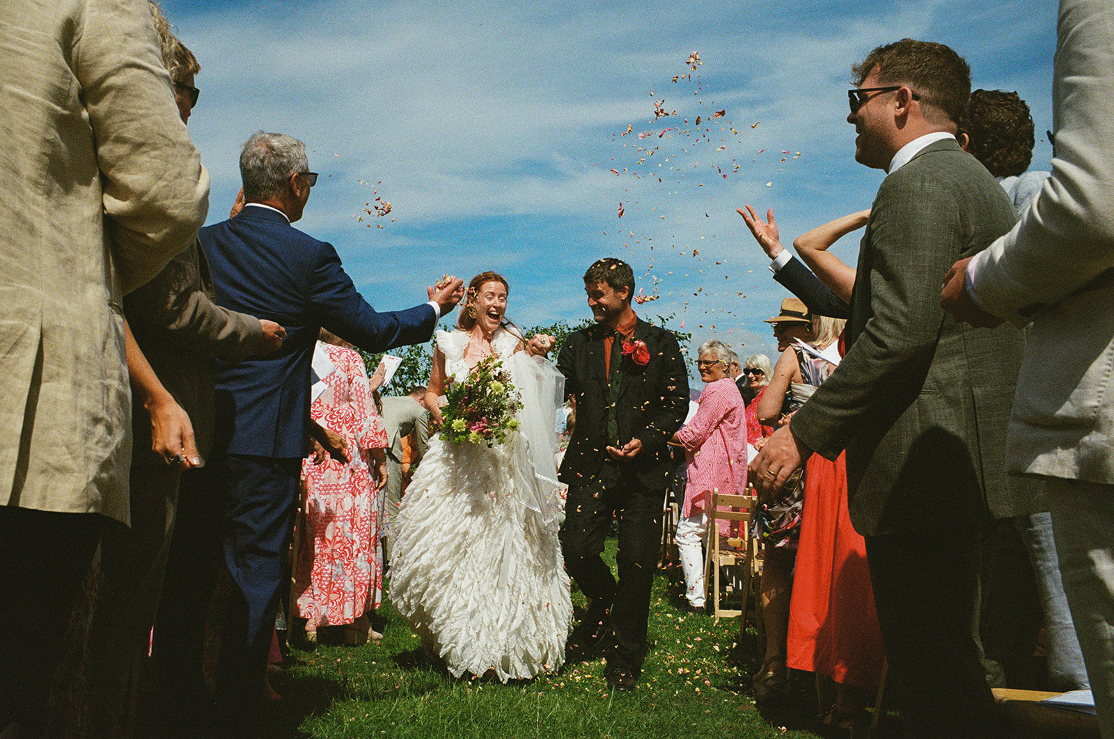 Newlyweds walk between their guests as petal confetti is thrown. Film wedding photography by York Place Studios