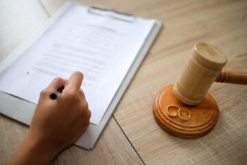 a hand with a pen writing notes in a folder, alongside a gavel