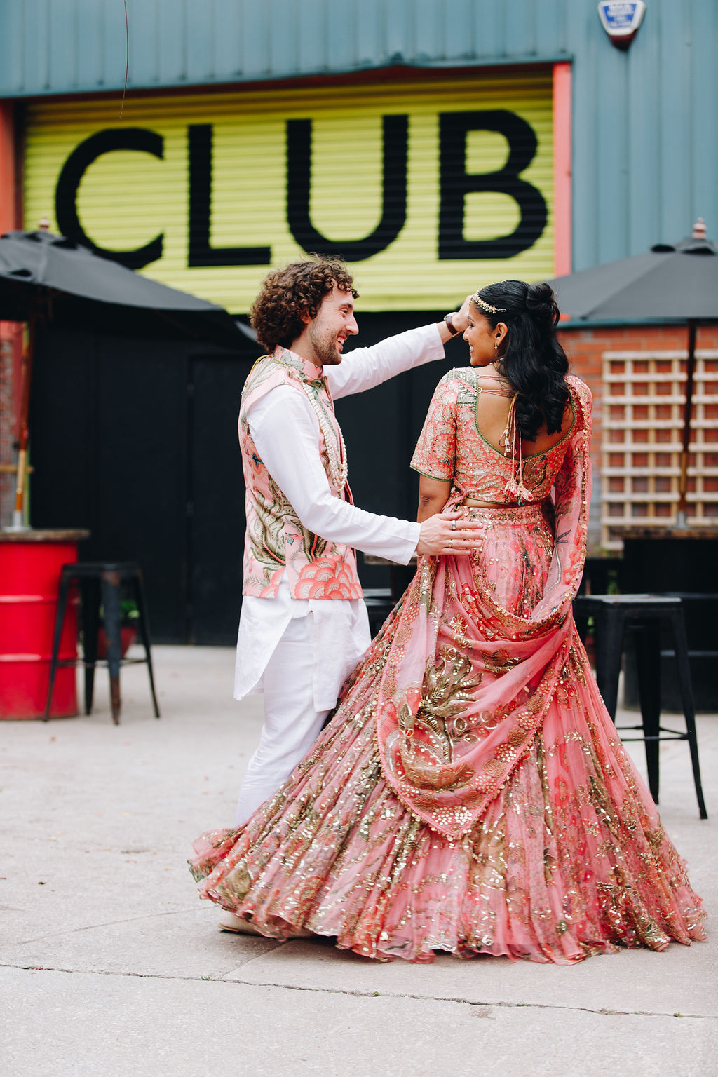 Groom and bride in Indian attire dancing outside a doorway with CLUB written above it in big bold letters | Priti Shikotra Weddings
