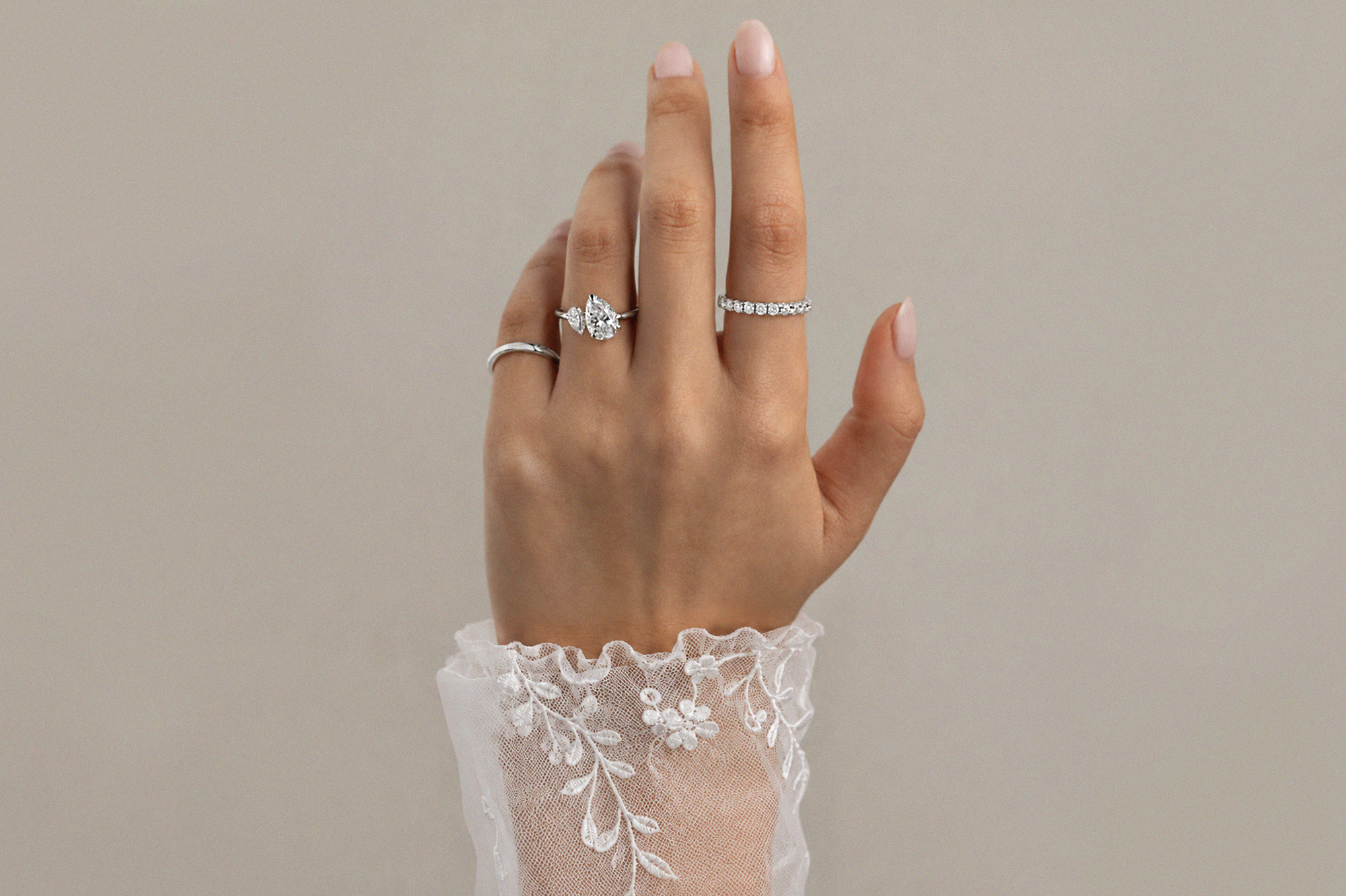 A feminine hand with elegant bespoke rings on 3 fingers, and a delicate lace sleeve | Lena Cohen Fine Jewellery London