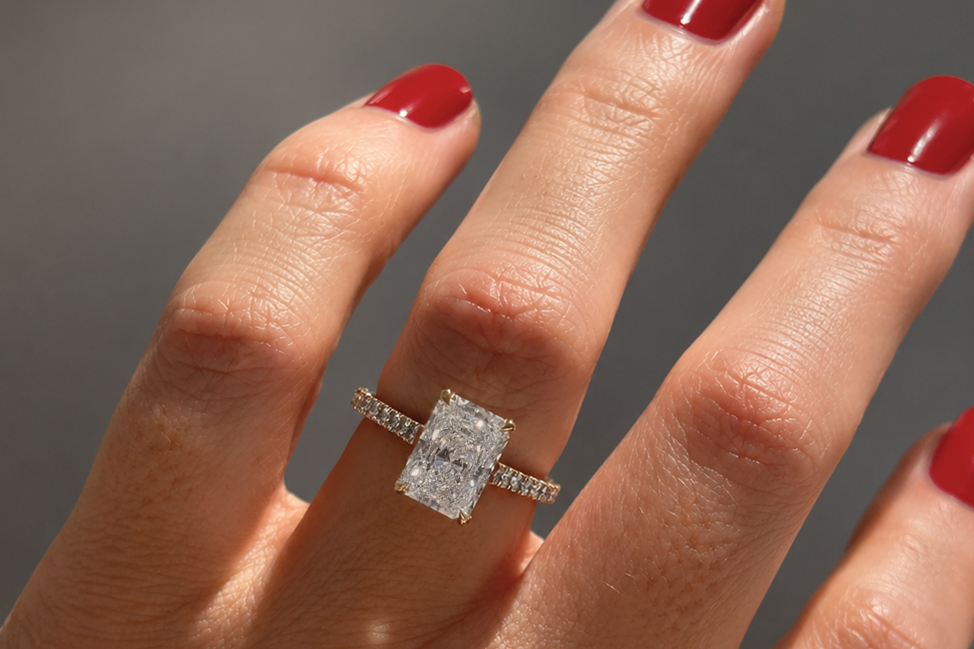Feminine hand with red nails wearing rectangle cut diamond engagement ring | Lena Cohen Fine Jewellery London